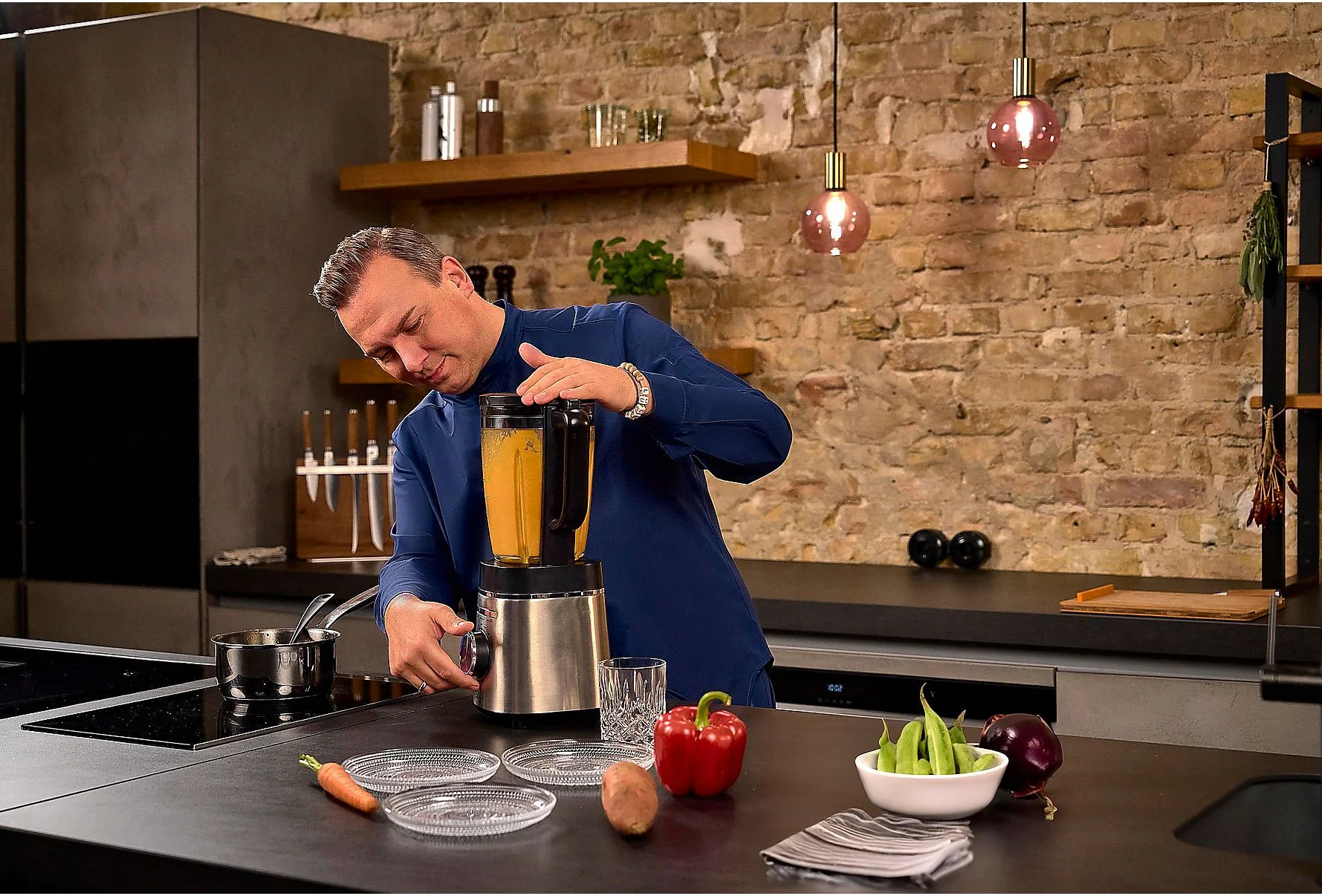 Mężczyzna miksuje zupę w kuchni, ze składnikami na blacie.