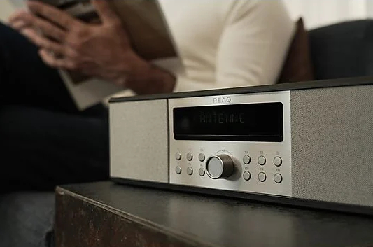 Radio na stole. Osoba czyta książkę w tle.