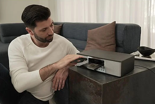 Mężczyzna wkłada kasetę do retro srebrnego systemu stereo na ciemnym stole.