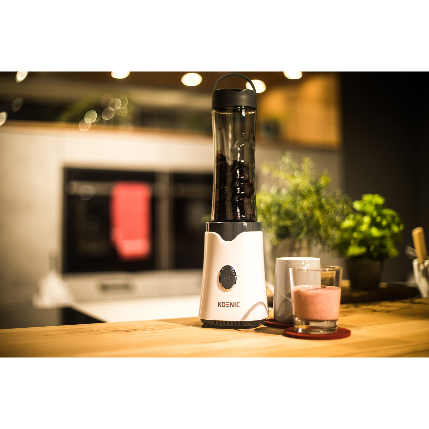 A white blender with a black lid is on a wooden counter. A glass and a mug are next to it.