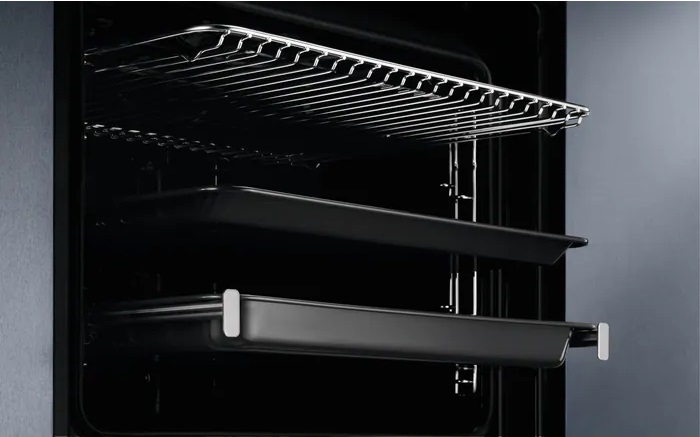 Wnętrze piekarnika z rusztami i tacami, pokazujące czystą i pustą przestrzeń.