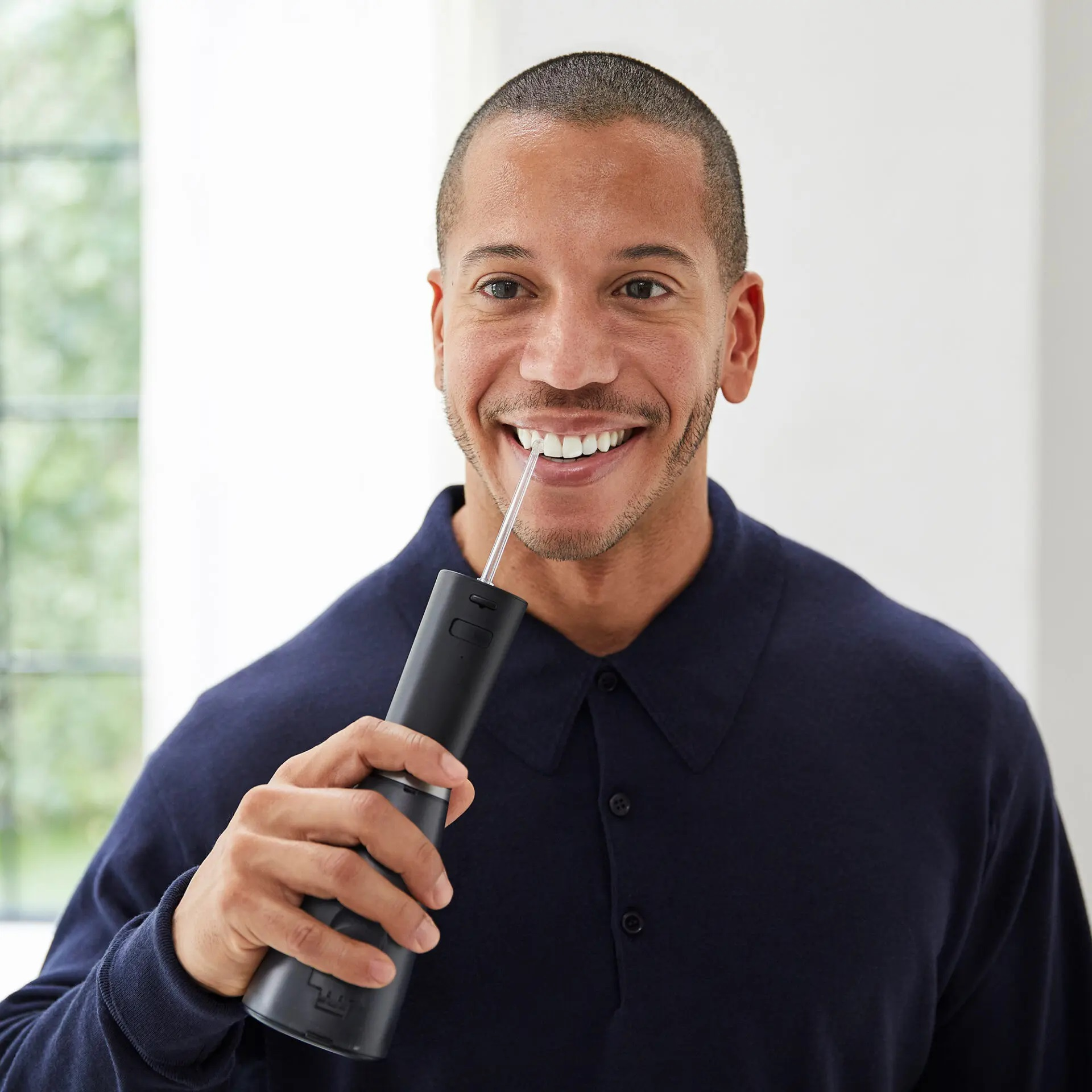 Mężczyzna z krótkimi włosami uśmiecha się, trzymając czarny irygator elektryczny, pokazując końcówkę.