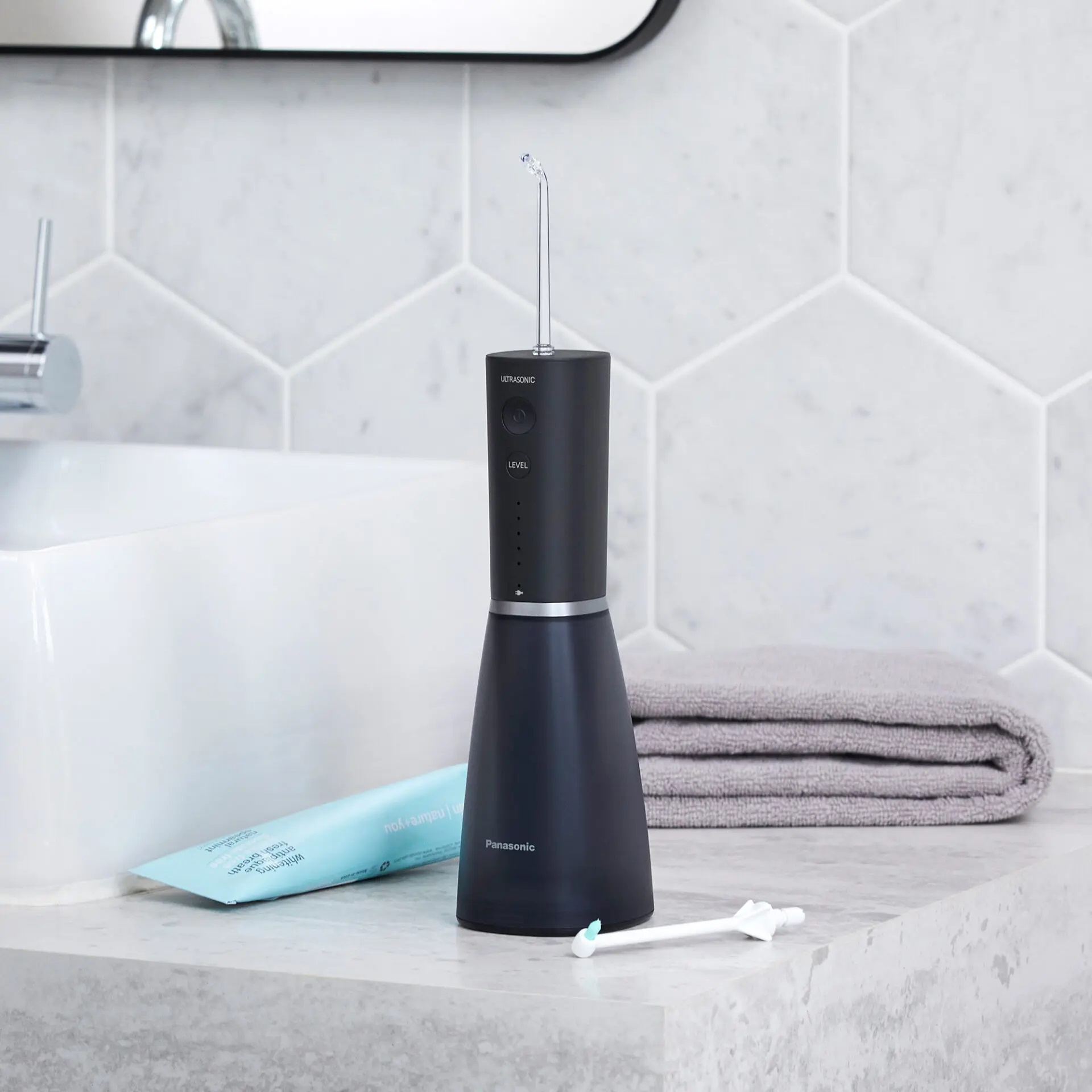 Czarny i srebrny irygator do jamy ustnej na marmurowym blacie, z pastą i ręcznikiem.