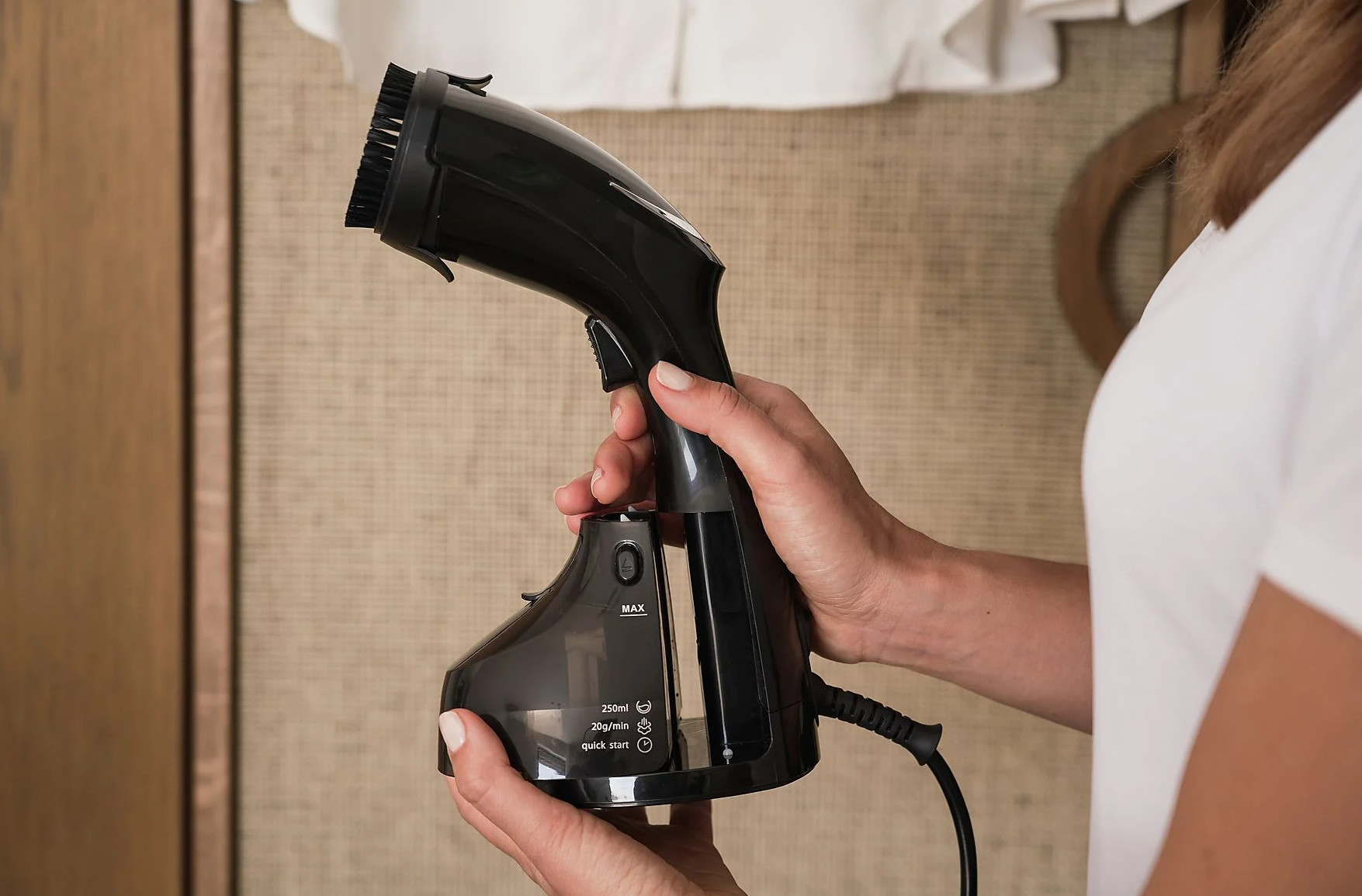 Kobieta trzymająca czarny ręczny parownik do ubrań. Widoczne szczegóły produktu.