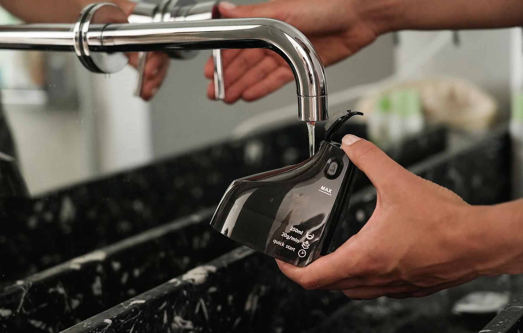 Osoba napełnia czarny zbiornik parownicy z kranu nad czarną marmurową powierzchnią.