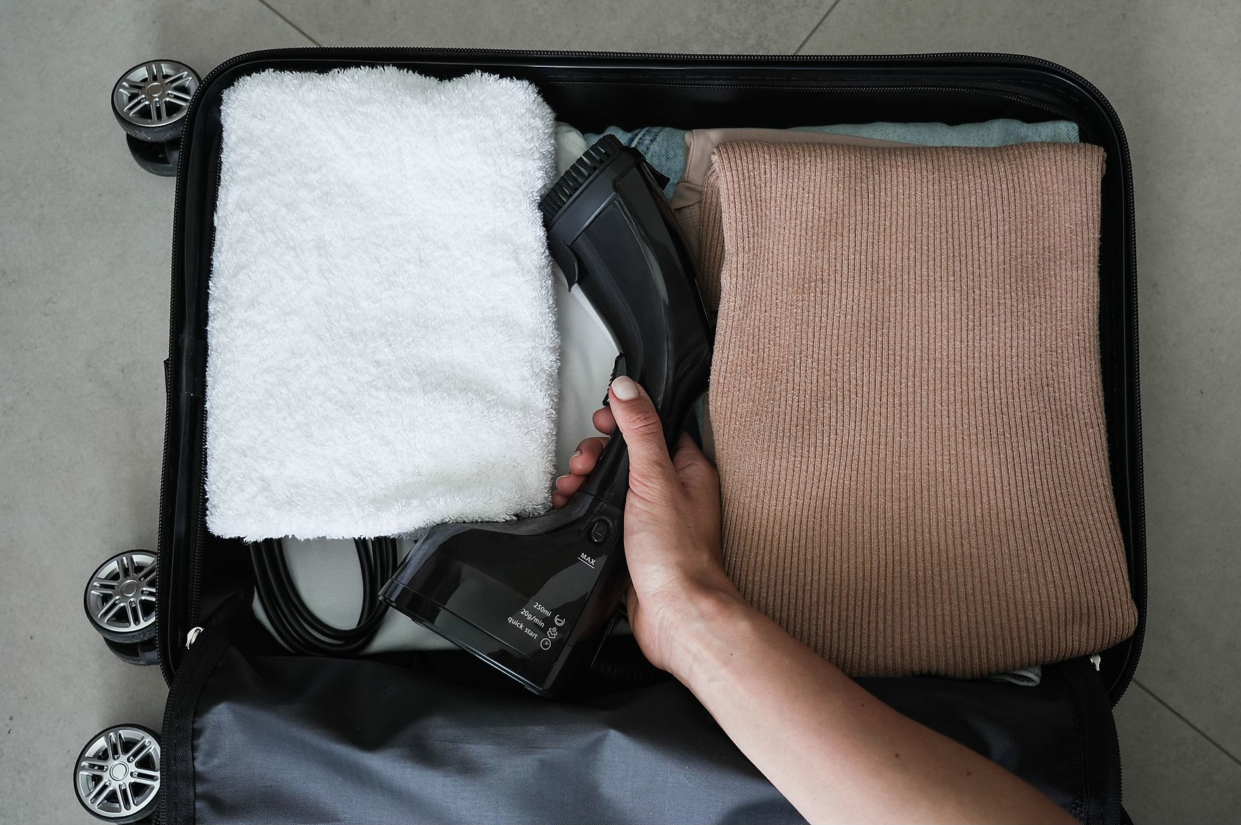 Otwarta walizka z ubraniami i czarną parownicą.