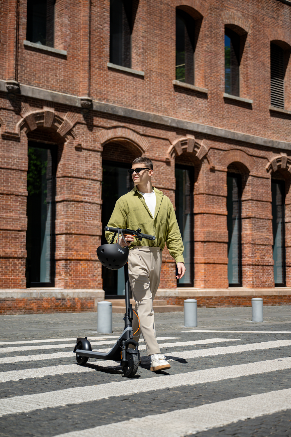 Hombre con gafas de sol y ropa casual camina con un patinete eléctrico.