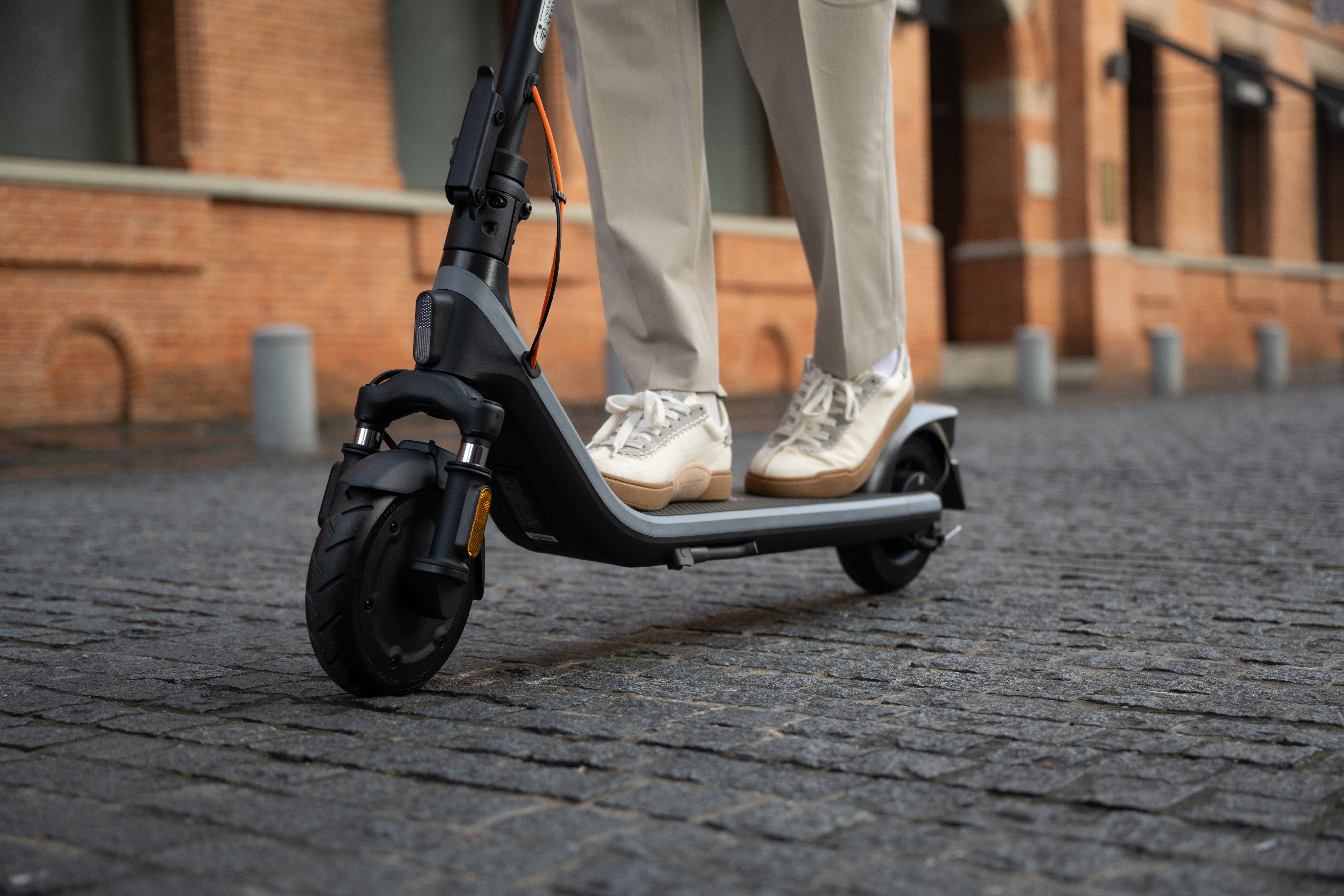 Una persona montando un scooter eléctrico en una calle adoquinada, con edificios de ladrillo detrás.