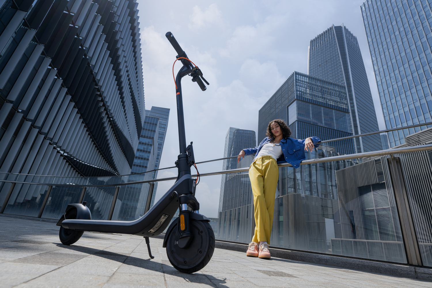 Una mujer se apoya en un edificio junto a un scooter. El scooter es negro y plateado.