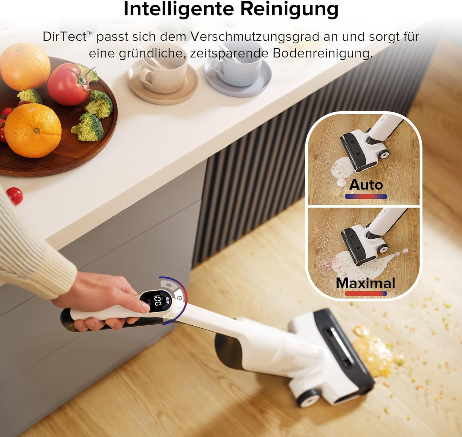Une personne utilise un aspirateur blanc sur le sol de la cuisine avec des fruits et légumes.