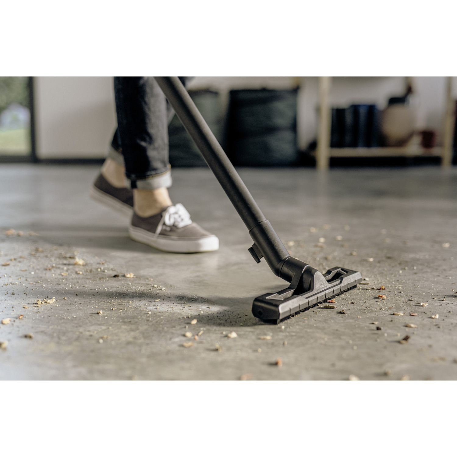 Person vacuuming a dirty floor with a vacuum cleaner, the floor has debris on it.