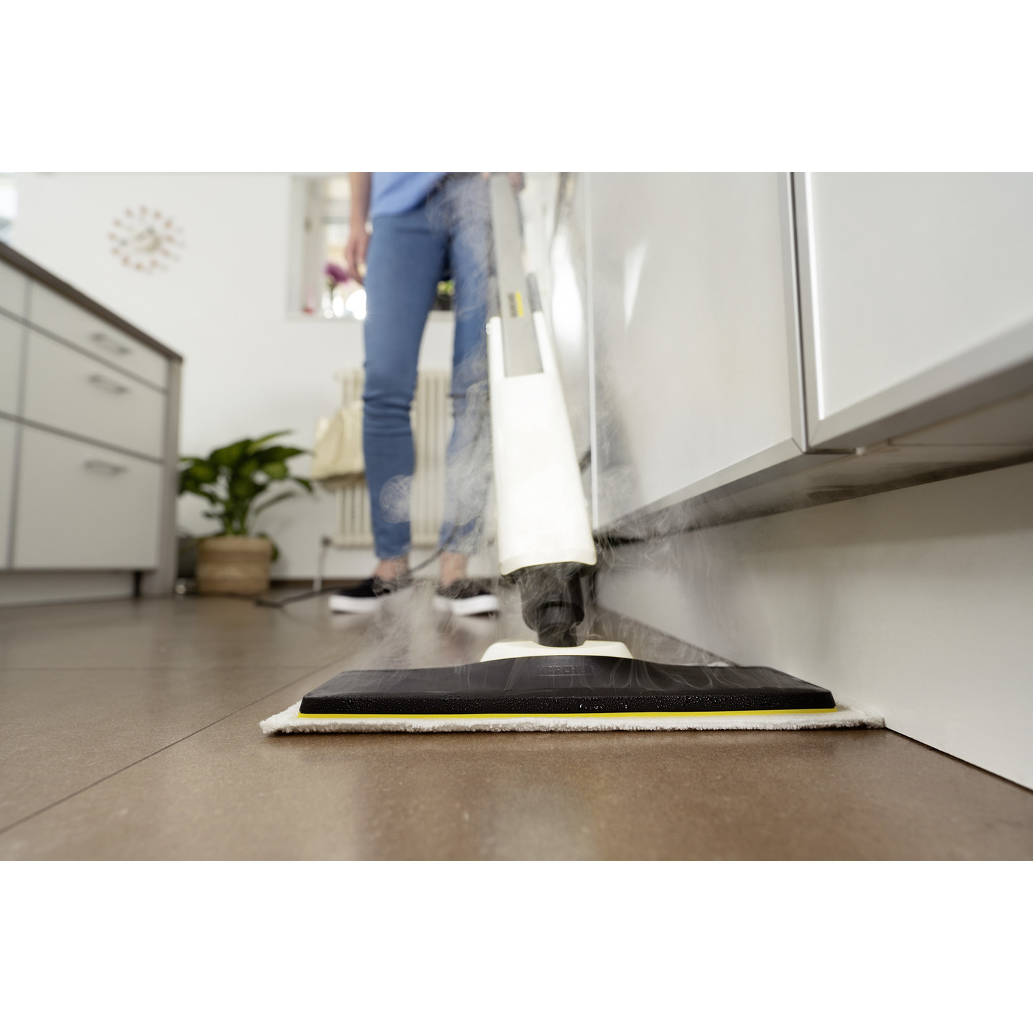Een persoon die een stoommop gebruikt op een bruine vloer. De mop is wit en zwart, schoonmakend bij een kast.