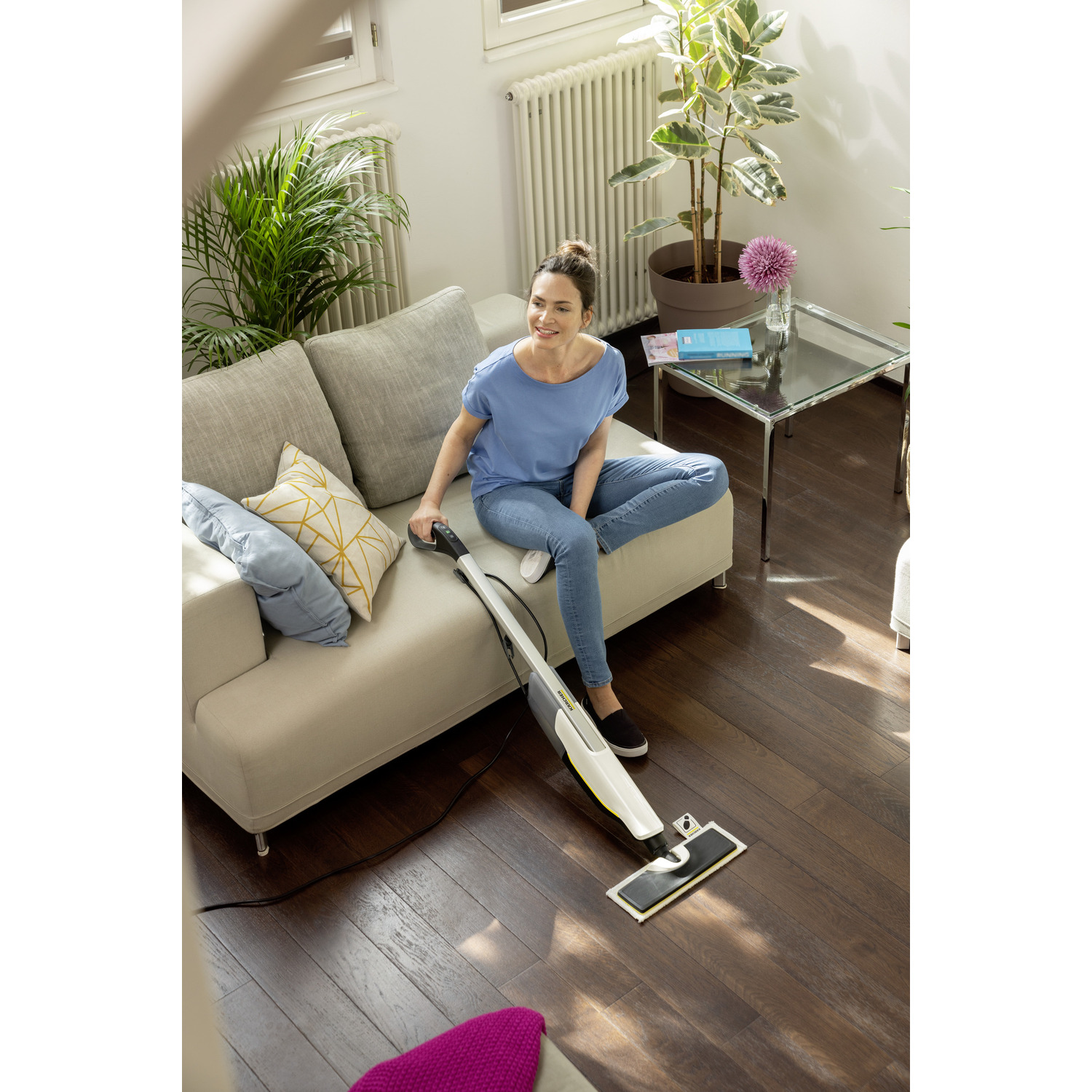 Vrouw gebruikt een stoommop op een houten vloer, zittend op een bank.