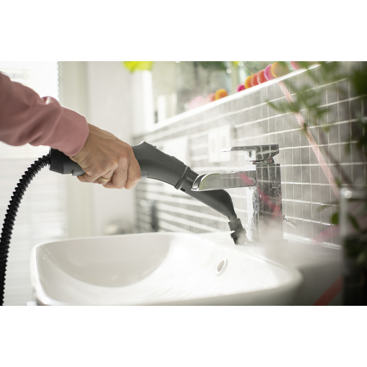 Hand holding a black and gray steamer over a white sink, with steam rising, in a bathroom.