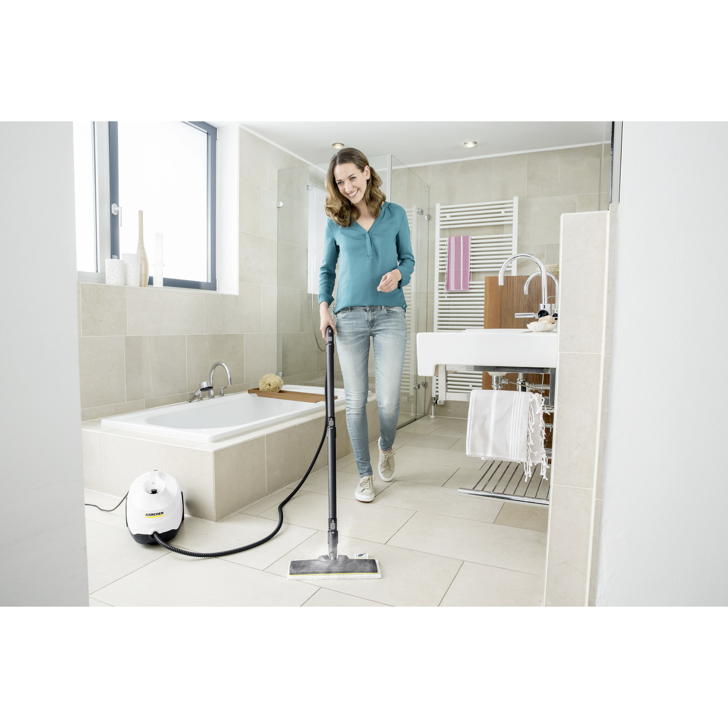 Woman using steam mop in a bathroom. White and beige tiles, a bathtub, and a sink are visible.