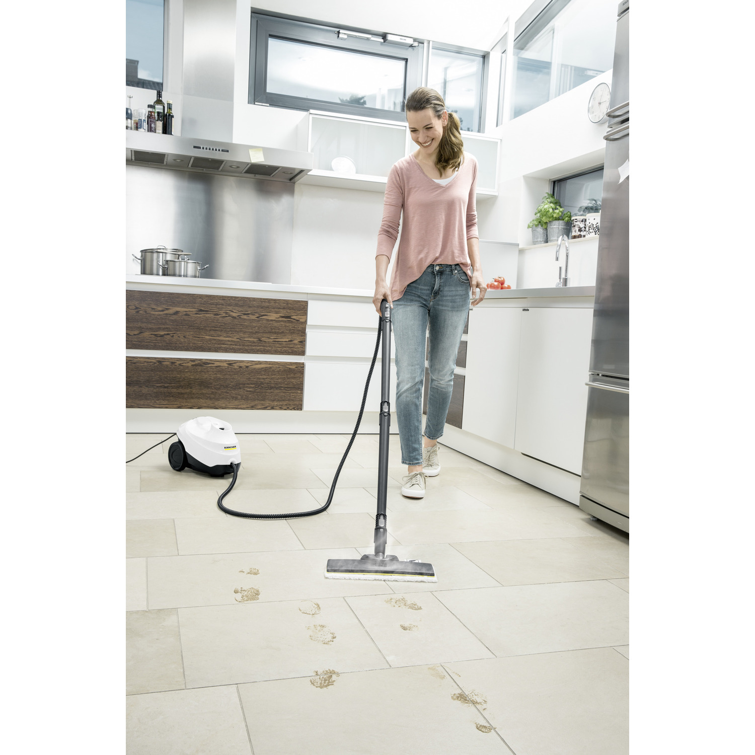 A woman using a steam cleaner on a tiled floor, leaving clean areas and dirty footprints.