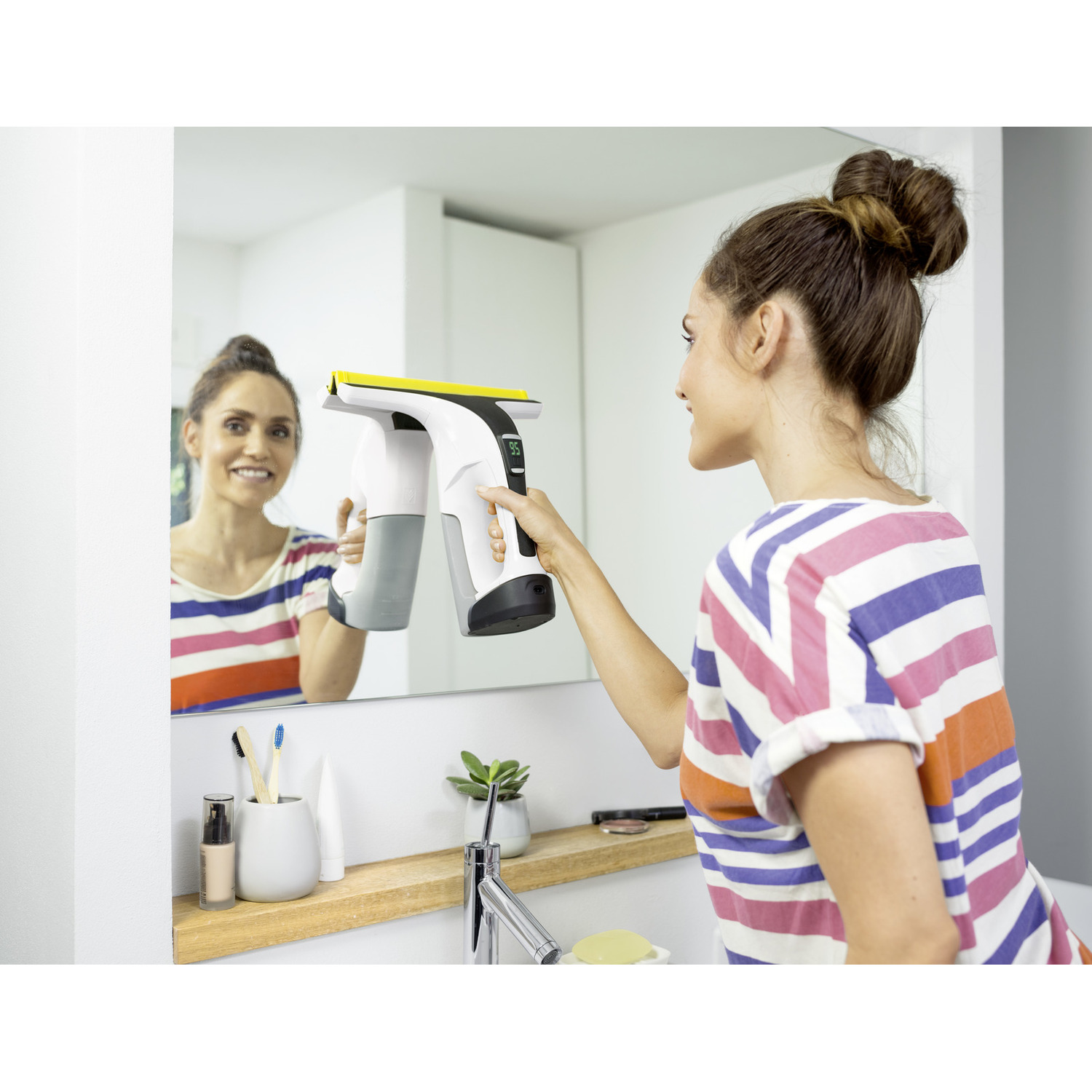 Een vrouw die een spiegel schoonmaakt met een schoonmaakapparaat dat ze vasthoudt.