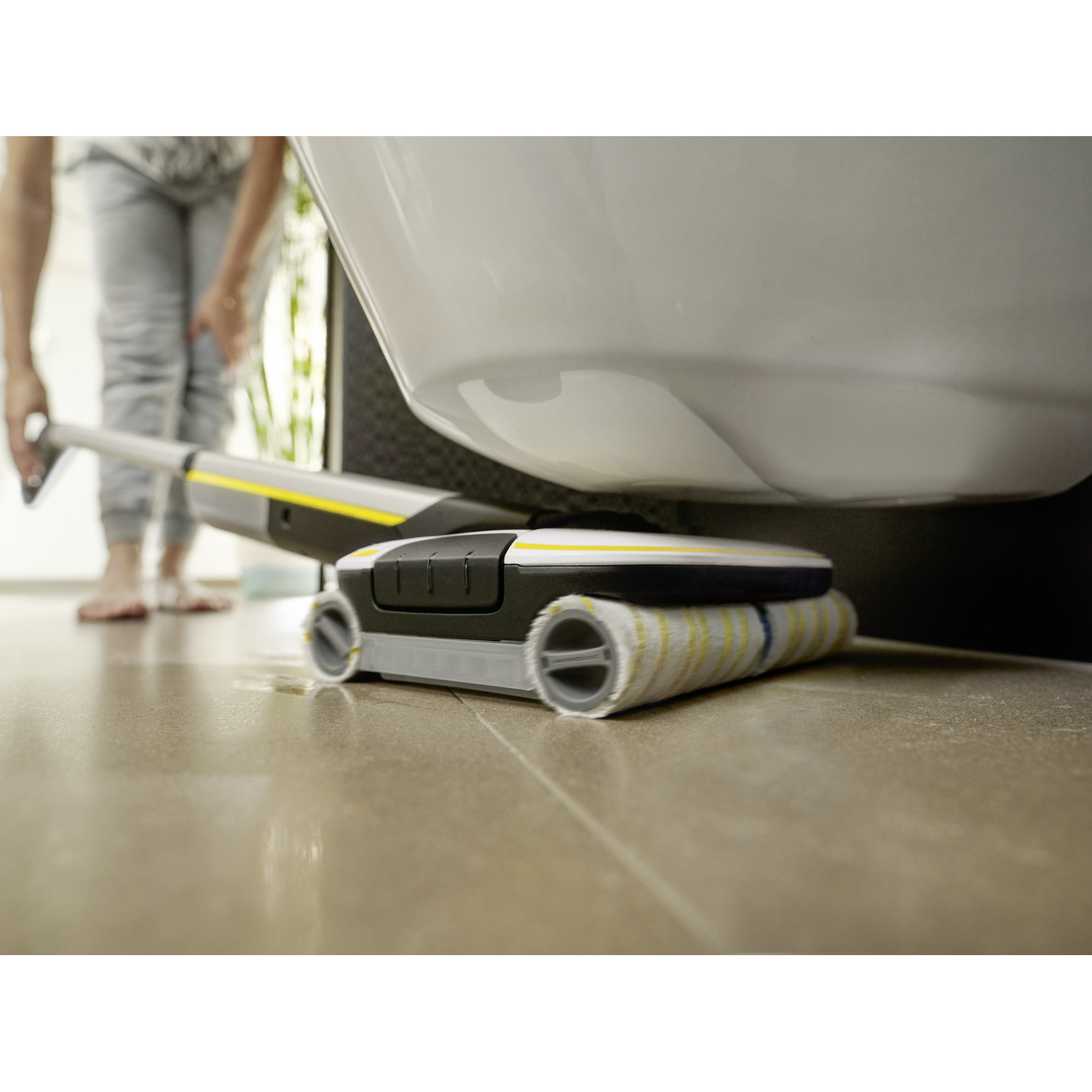 A cleaning device under a toilet, cleaning the floor. The device is yellow and black.