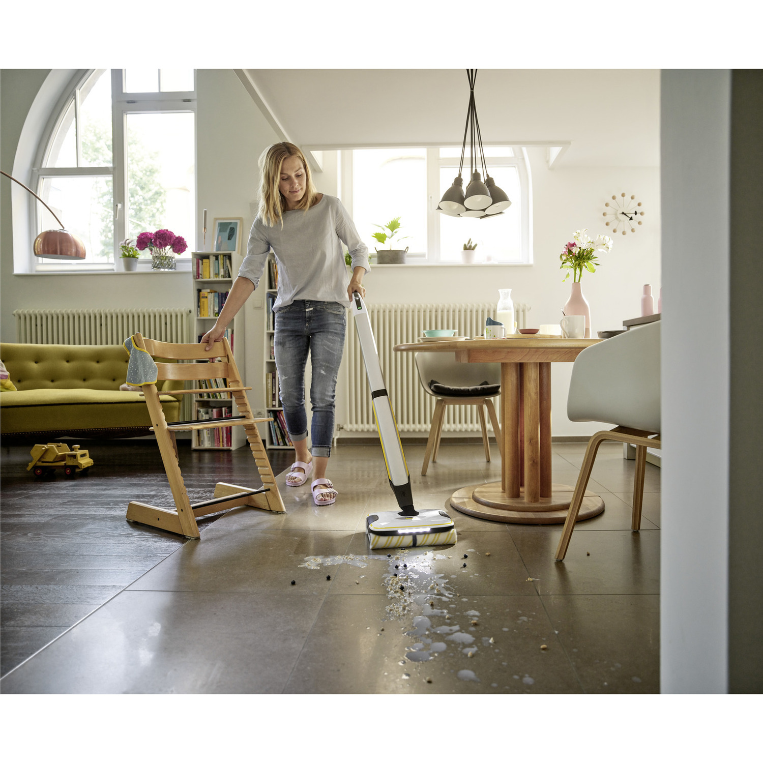 Vrouw die de vloer schoonmaakt met een witte Kärcher. Kinderstoel en tafel op de achtergrond.