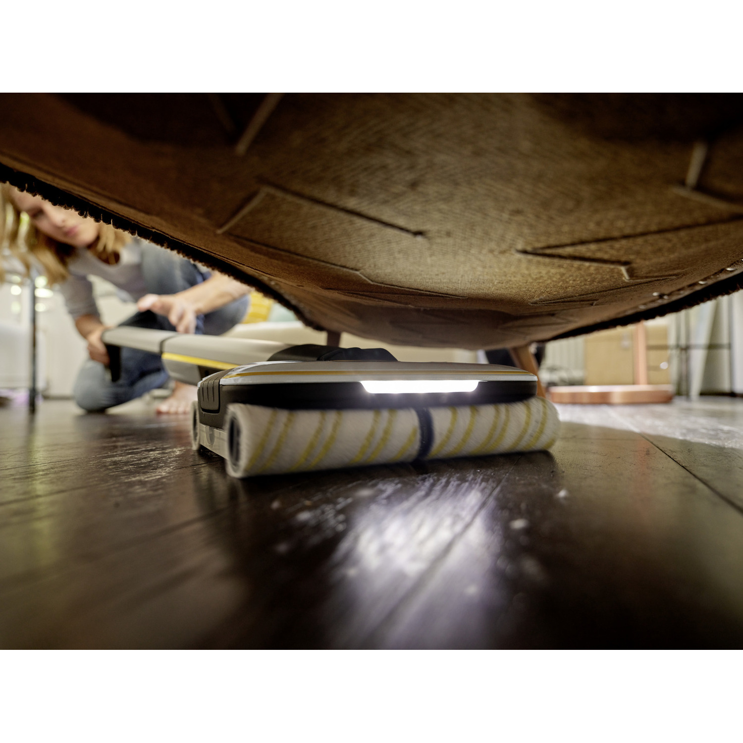 Een persoon gebruikt een schoonmaakapparaat onder een kleed op een houten vloer.