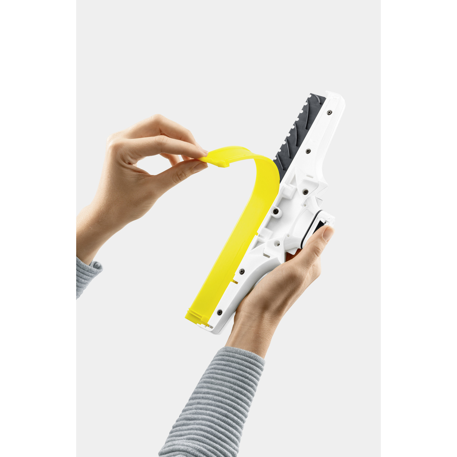Hands peeling a yellow protective strip from a white and black device. Grey background.