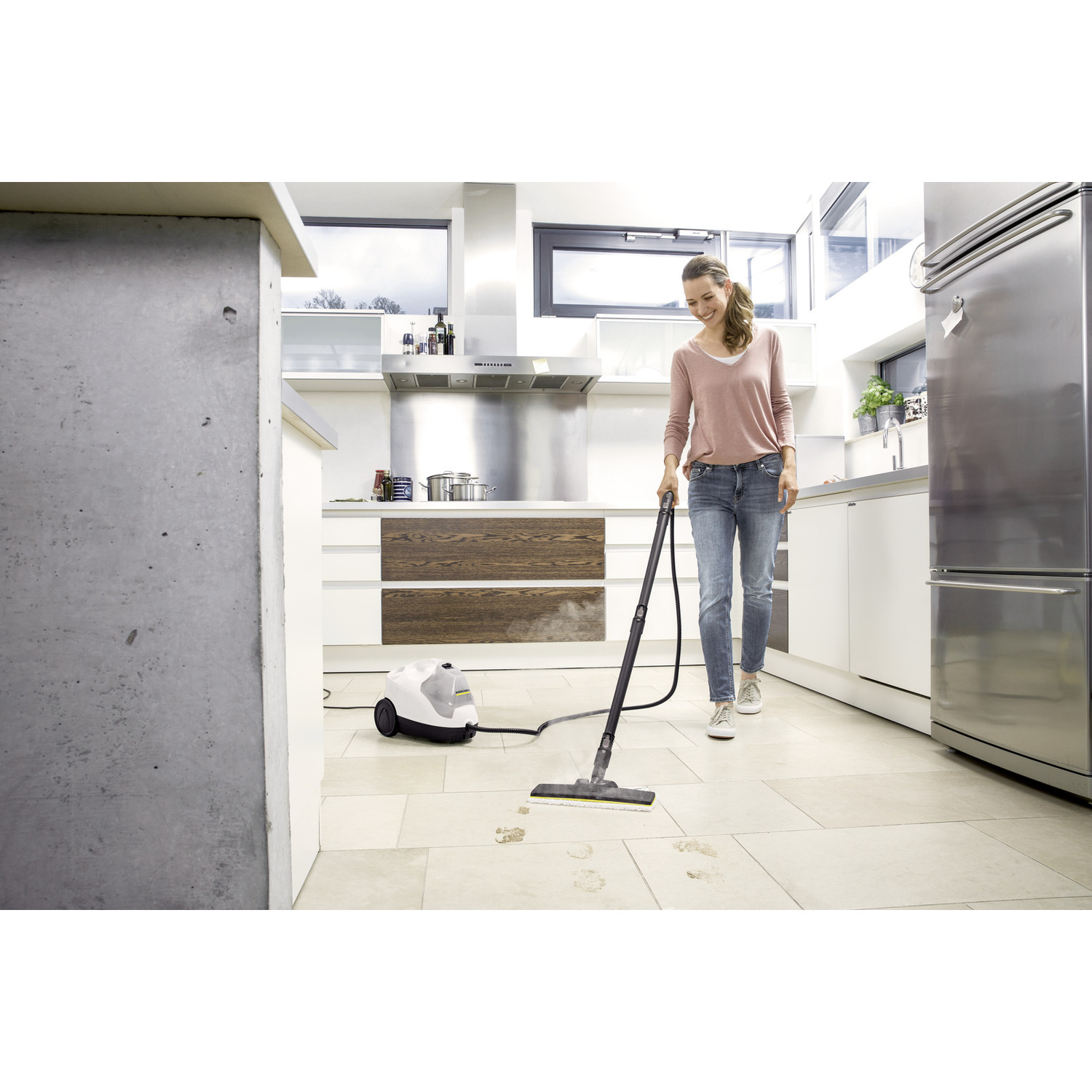 Een vrouw gebruikt een stoomreiniger op een tegelvloer in een keuken.