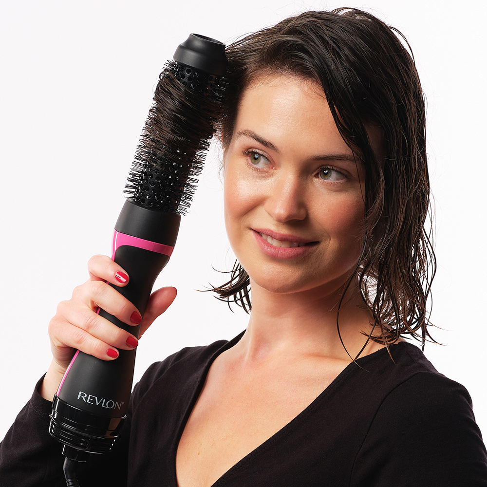 Frau benutzt eine Revlon-Haartrocknerbürste auf nassem Haar. Rosa-schwarzes Gerät. Weißer Hintergrund.