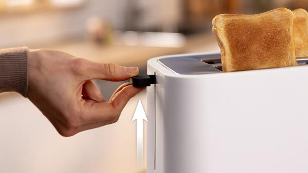 Eine Hand hebt den Hebel eines weißen Toasters an, um den Toast anzuheben.