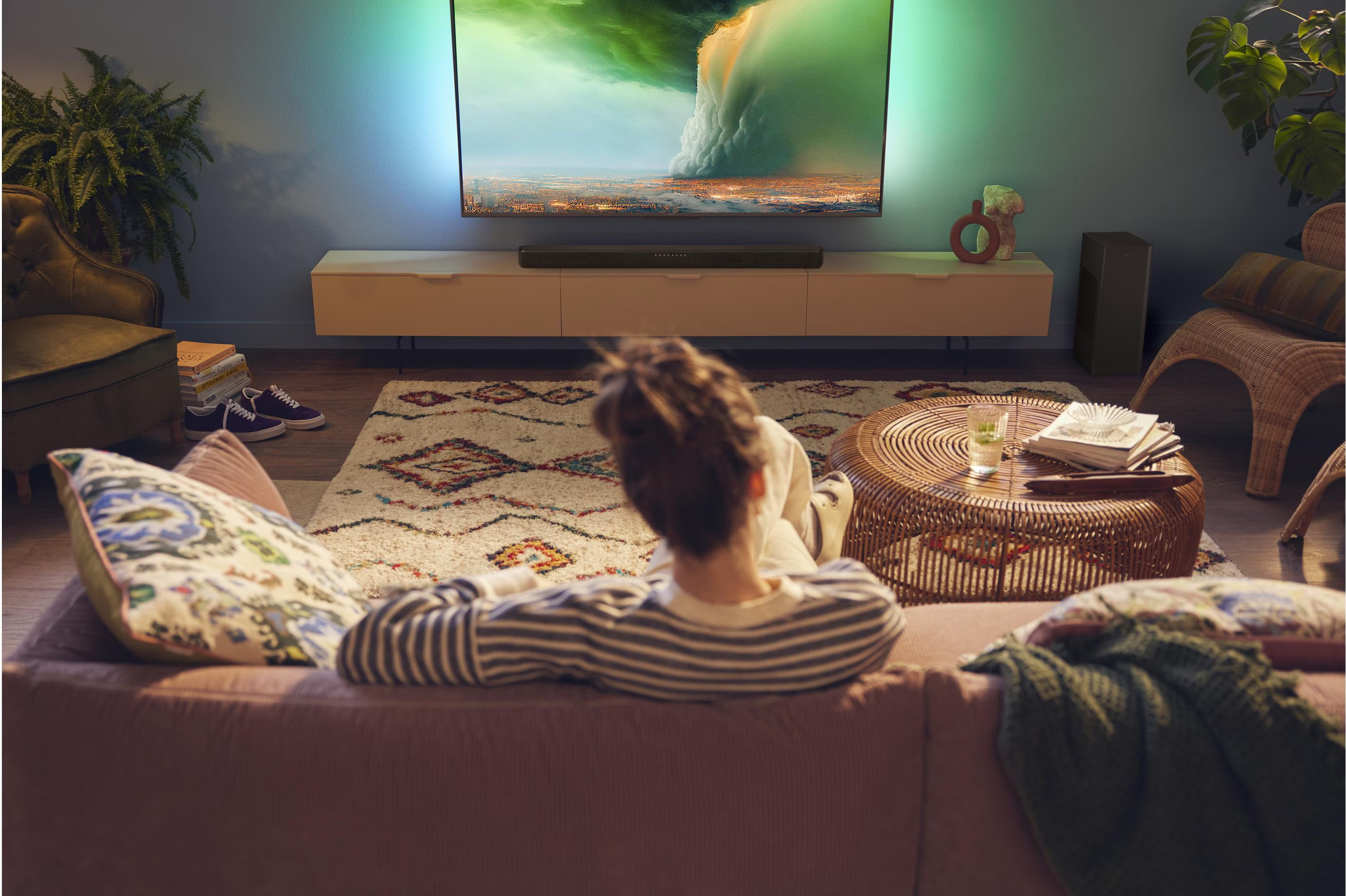 Una persona che guarda la TV in un soggiorno. La TV è montata su un mobile bianco e ha delle luci.
