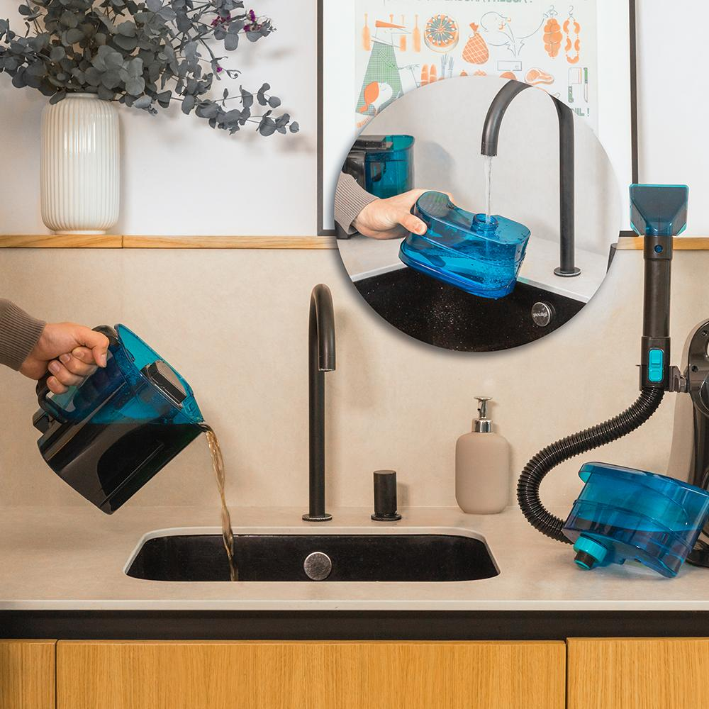 Manos vertiendo agua en un dispositivo de limpieza azul, con un fregadero y grifo negros.