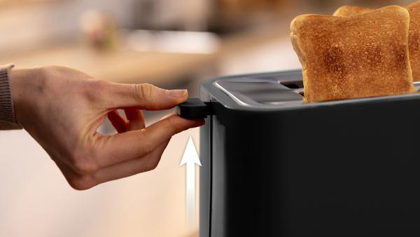 Eine Hand zieht einen Hebel, um Toast aus einem schwarzen Toaster zu heben.