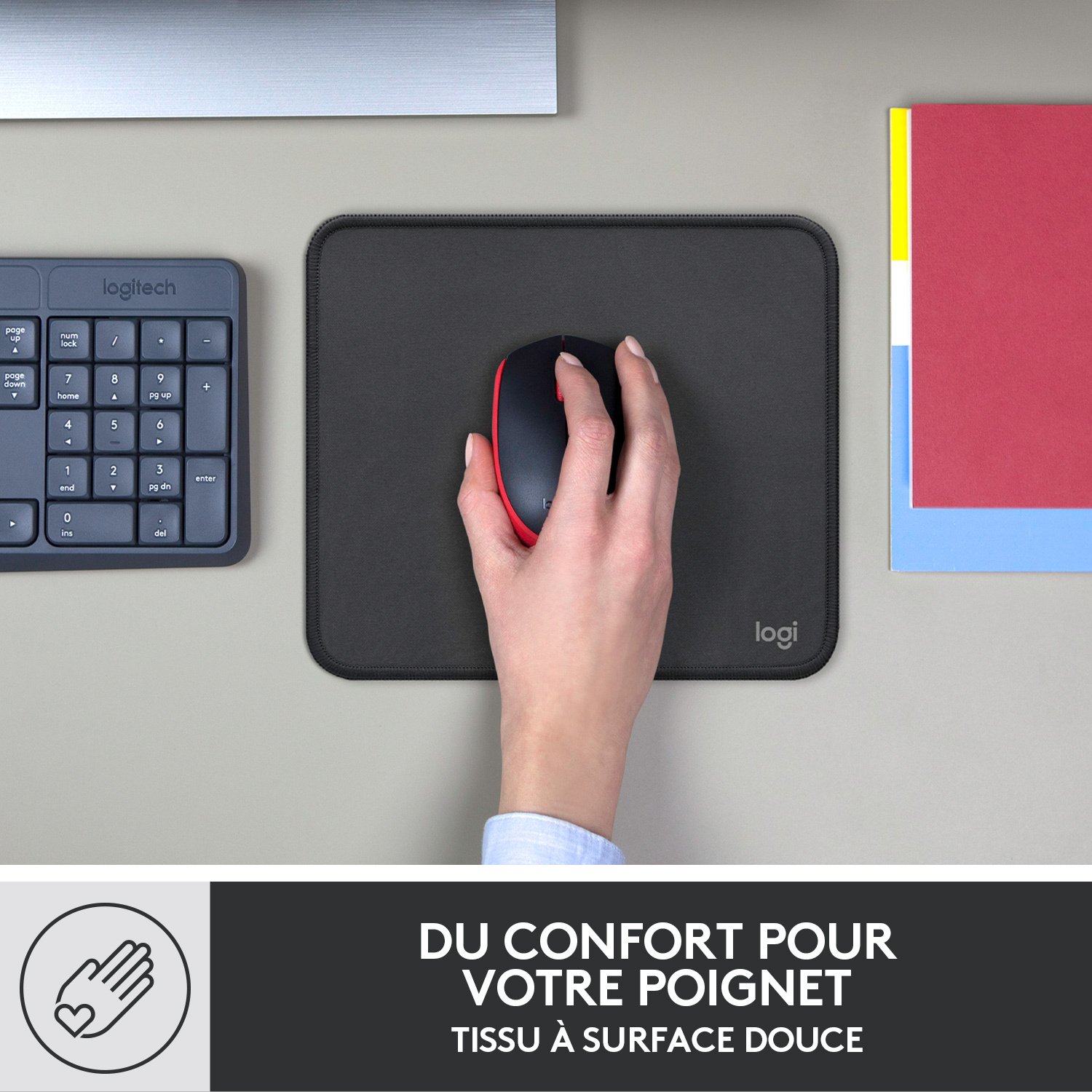 Une main repose sur un tapis de souris noir; une souris sans fil et un pavé numérique sont visibles.
