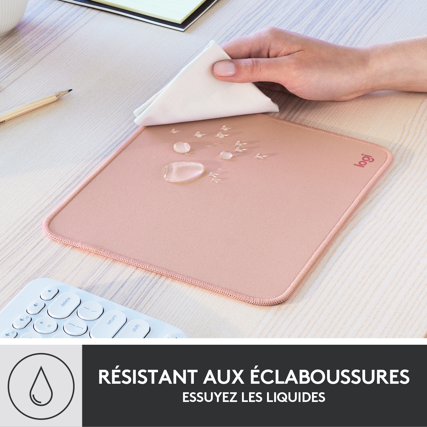 Un tapis de souris rose avec des gouttes d'eau essuyées par un chiffon blanc sur un bureau en bois, clavier blanc en dessous.