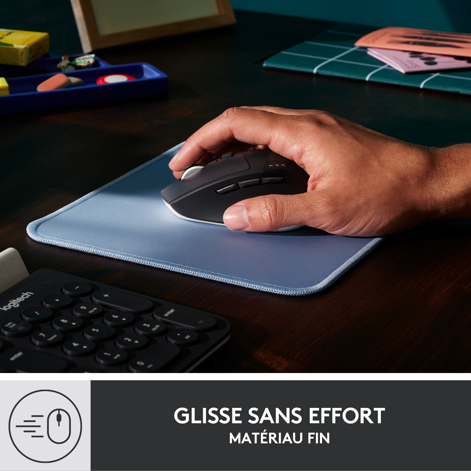 Une main utilise une souris noire et blanche sur un tapis de souris bleu, avec un clavier en arrière-plan.