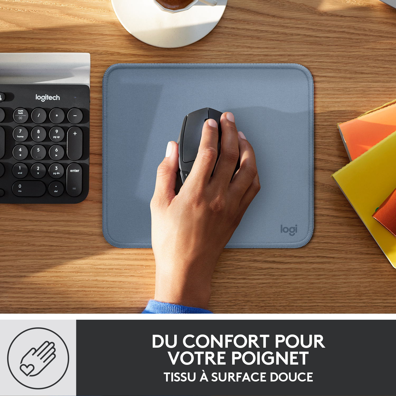 Une main utilise une souris noire sur un tapis de souris bleu, à côté d'un clavier et d'autres objets.