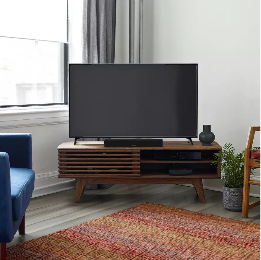 Wohnzimmer mit Fernseher auf einem Holzständer, Teppich, blauem Stuhl und Fenster.