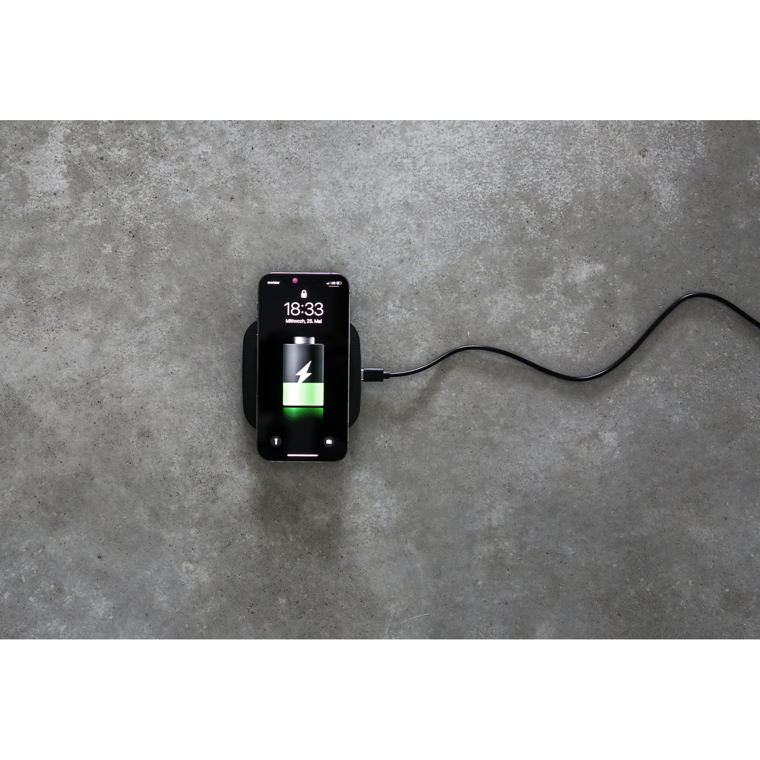 Zwarte telefoon laadt op zwarte draadloze oplader. Batterij laadt. Grijs oppervlak.