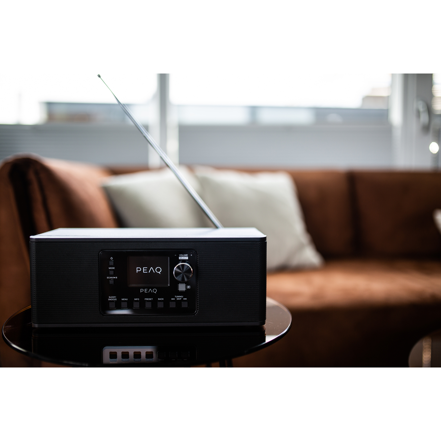 Black PEAQ radio on a table with a sofa in the background. The radio has a screen.