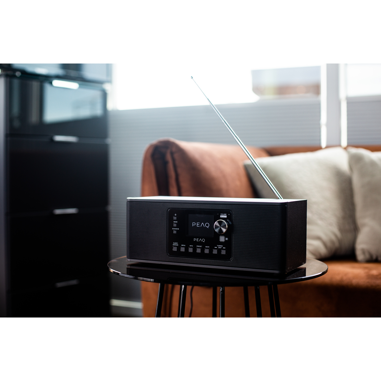 Black PEAQ radio on a table with a brown sofa in the background.