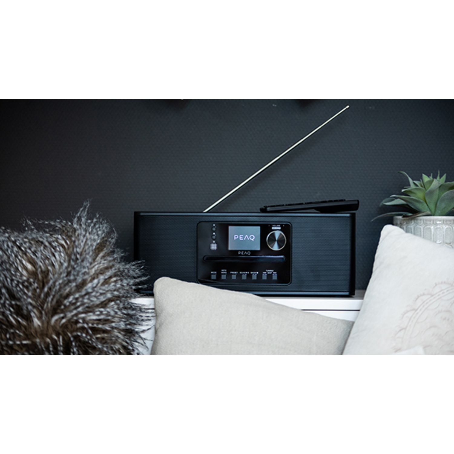 A black radio with a small display and a remote control on a white surface.