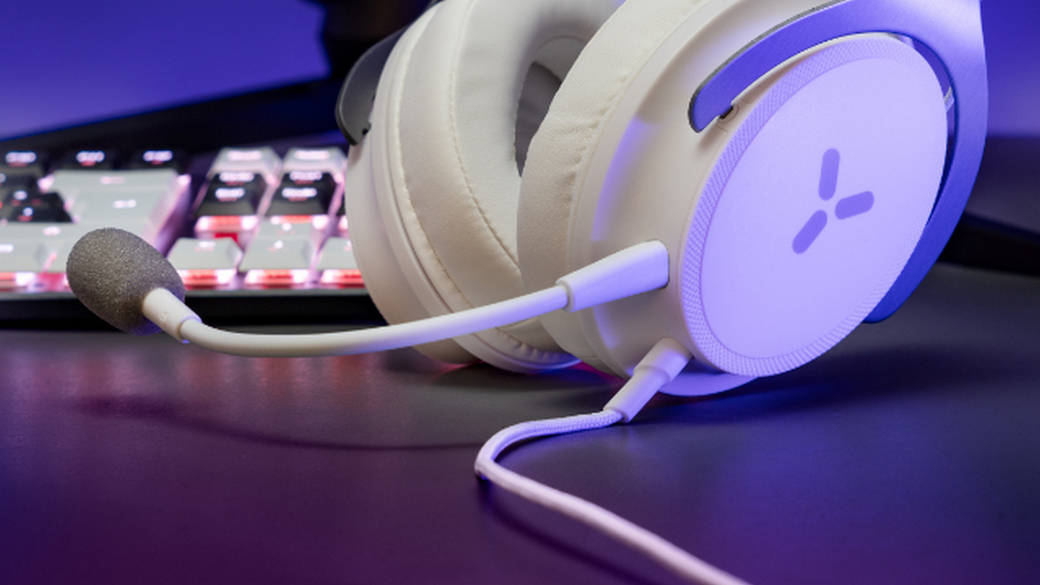 Auriculares gaming blancos con micrófono sobre superficie negra, teclado en el fondo.