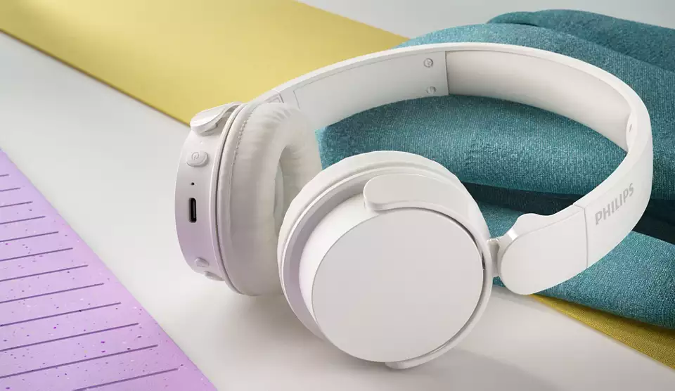 Renkli kumaşların üzerinde duran, USB portlu beyaz Philips kulaklıklar.