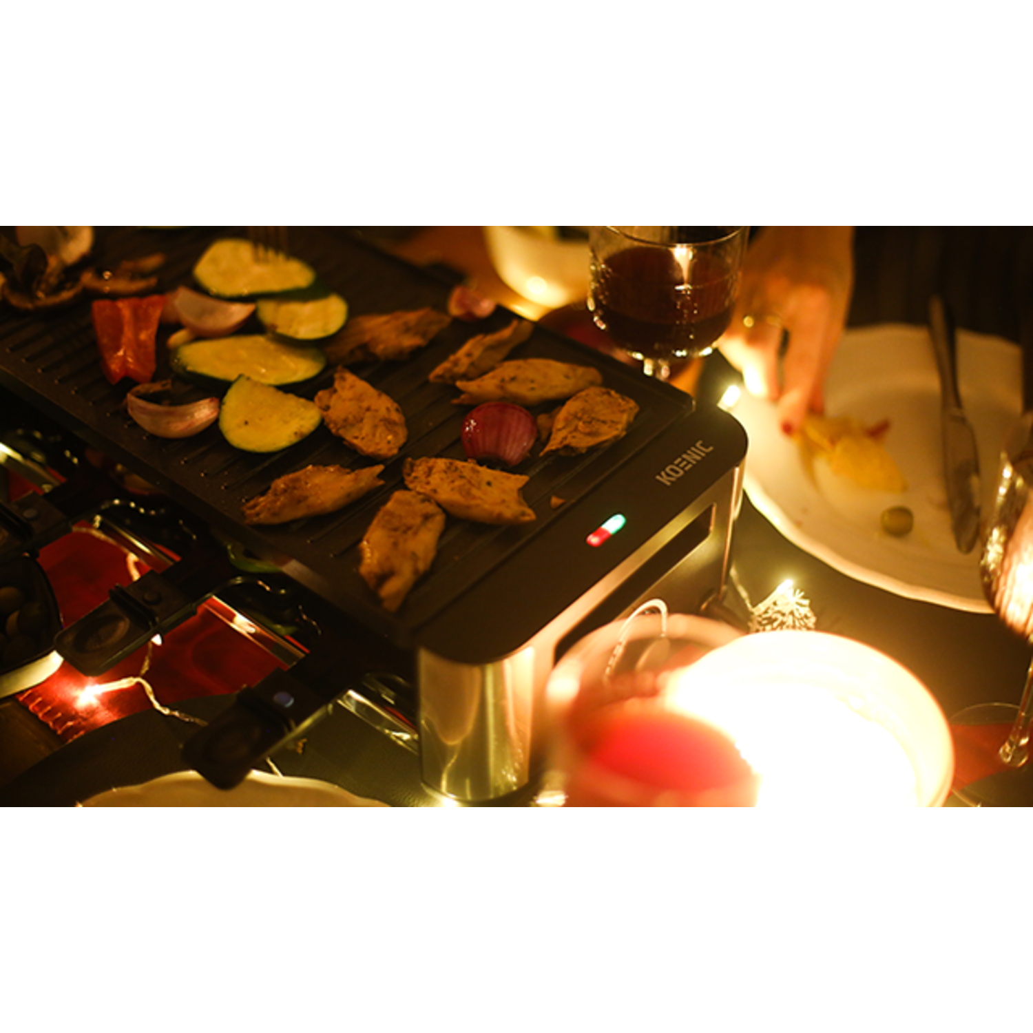A raclette grill with cooked food, candles, and a person's hand reaching.