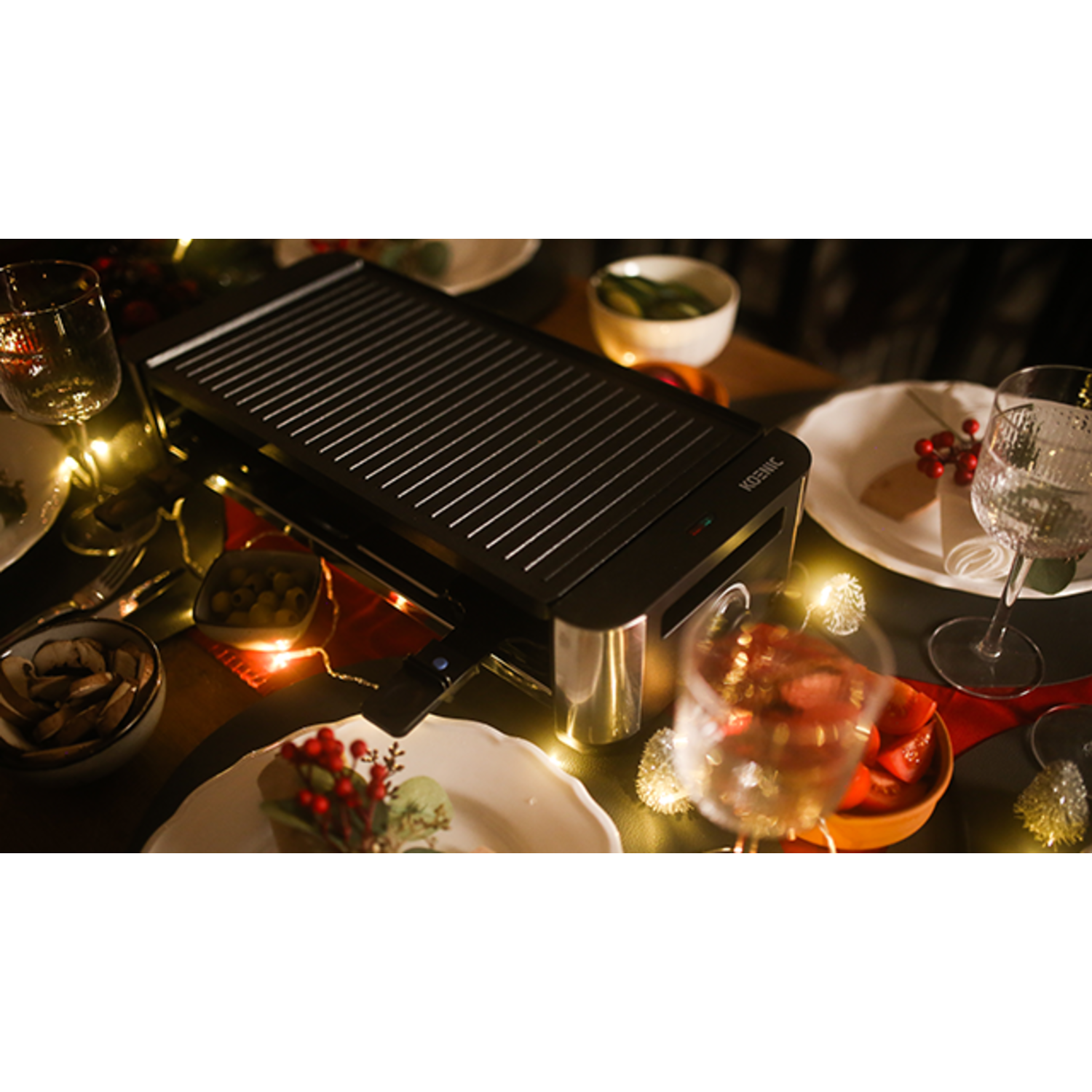 Black grilling machine with food on a table with lights and dishes.