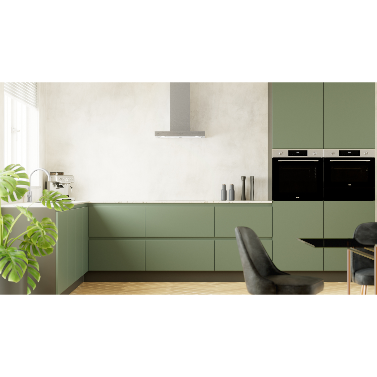 Green kitchen with cabinets, two ovens, and a stove hood. Plant in the foreground.