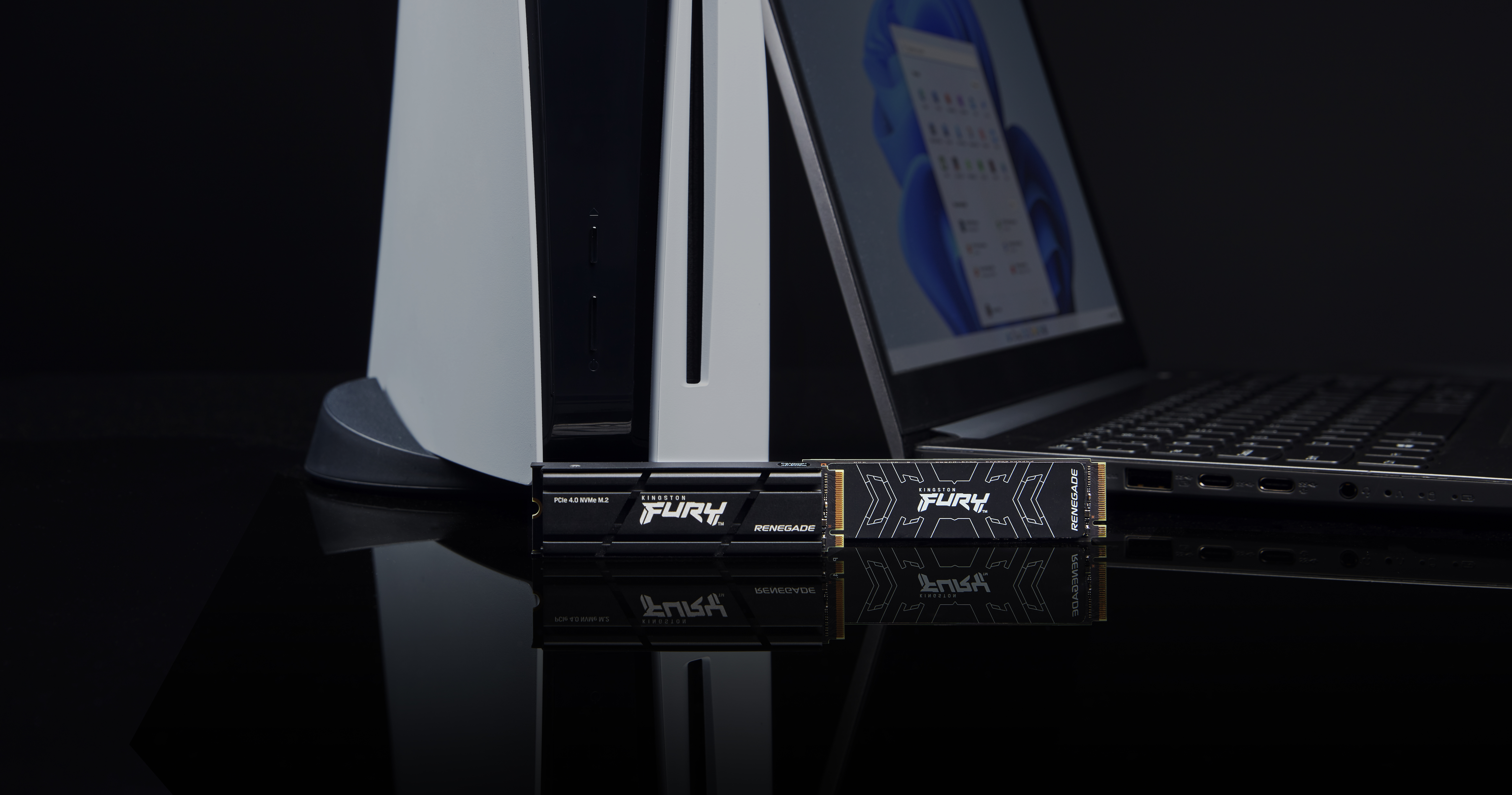 Zwei Kingston FURY Renegade SSDs, eine PS5 und ein Laptop auf einer reflektierenden schwarzen Oberfläche.