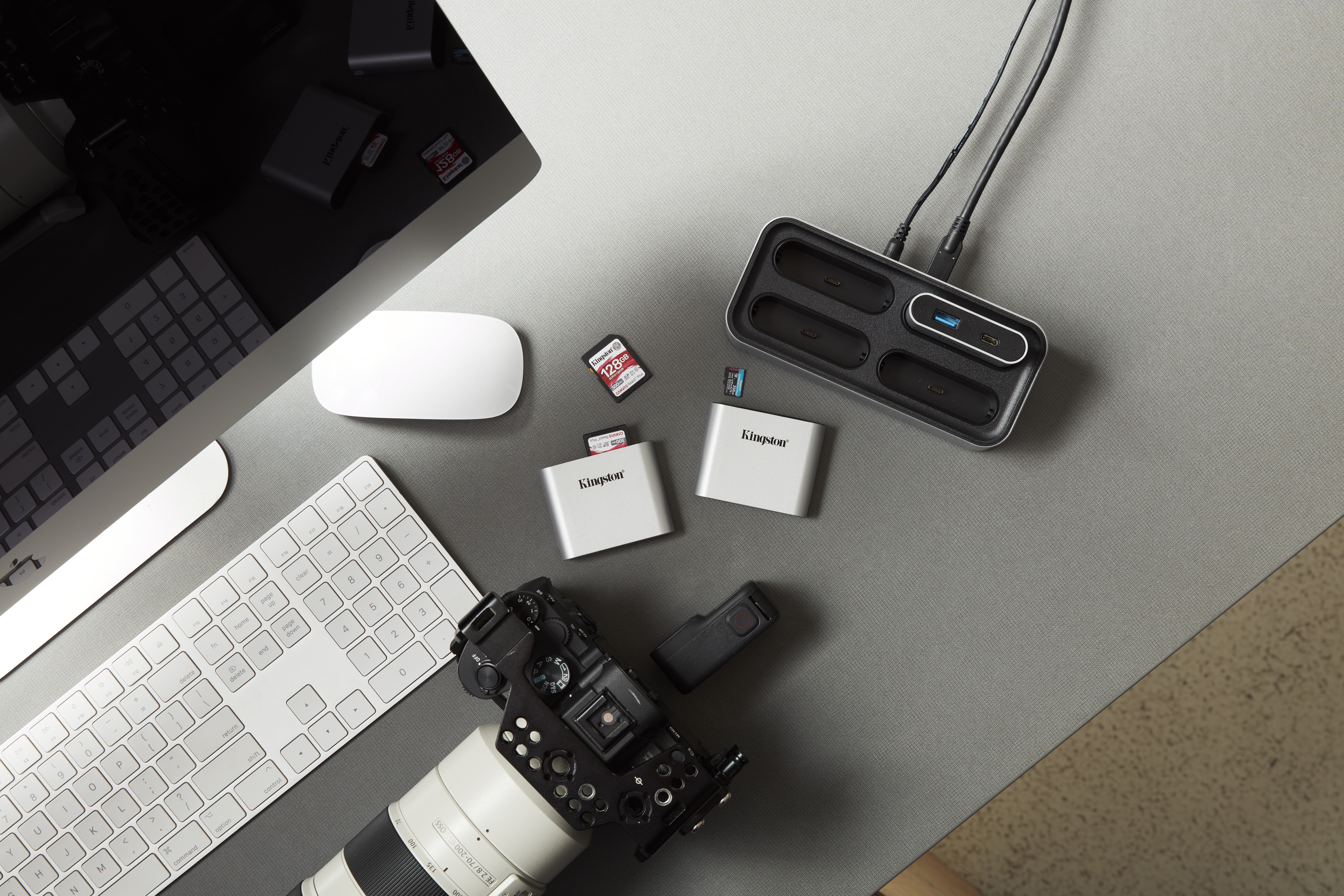 Ein Schreibtisch mit Computerausrüstung: Monitor, Tastatur, Maus, SD-Karten und Kamera.