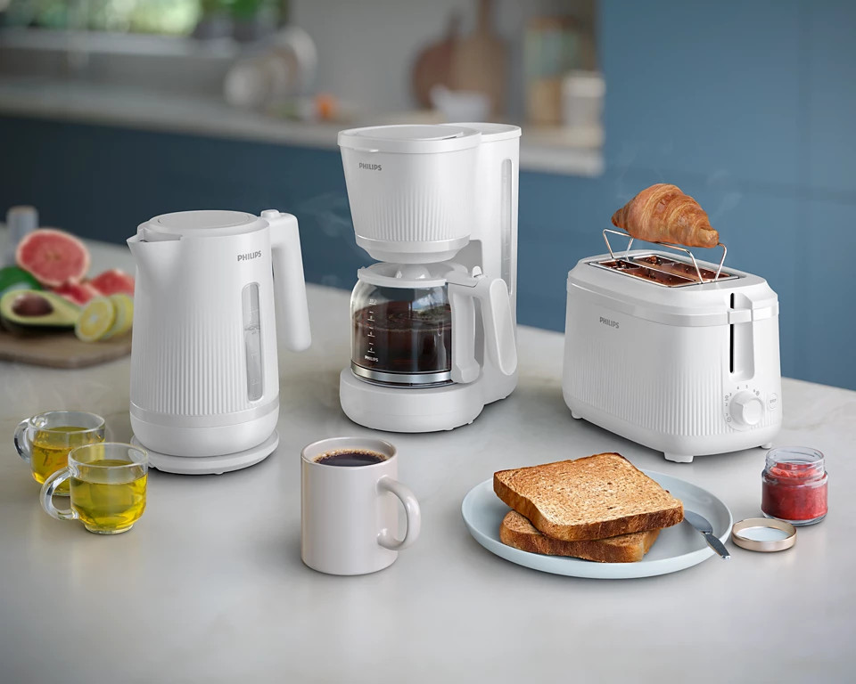 Białe urządzenia kuchenne z jedzeniem na stole. Zawiera czajnik, ekspres do kawy i toster.