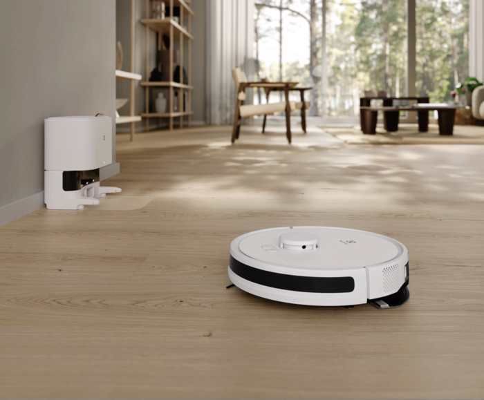 Fehér robotporszívó fa padlón, a nappaliban. A töltőállomás balra van.