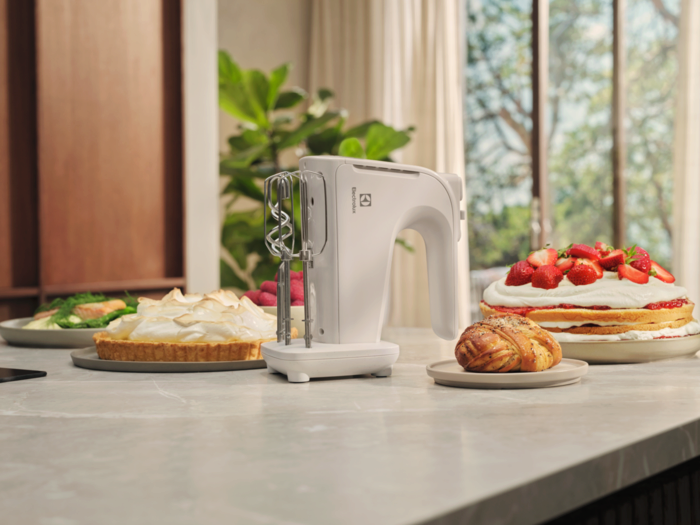 Fehér Electrolux kézi mixer tartozékokkal és süteményekkel a pulton.